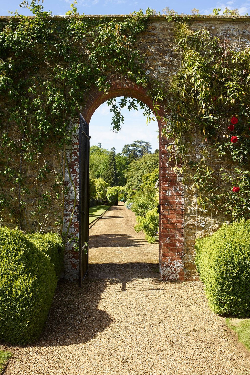 A red brick archway overhung with roses and clematis links two garden rooms.