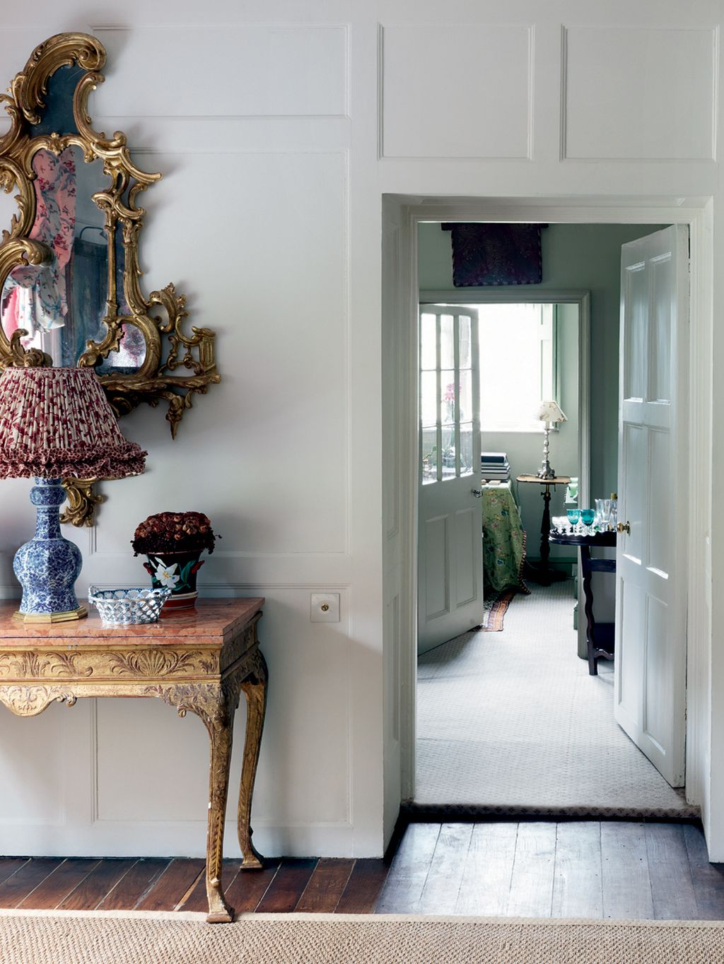 The drawing room is painted in 'Cornforth White' by Farrow  Ball. A door flanked by one of a pair of rococo gilt mirrors...