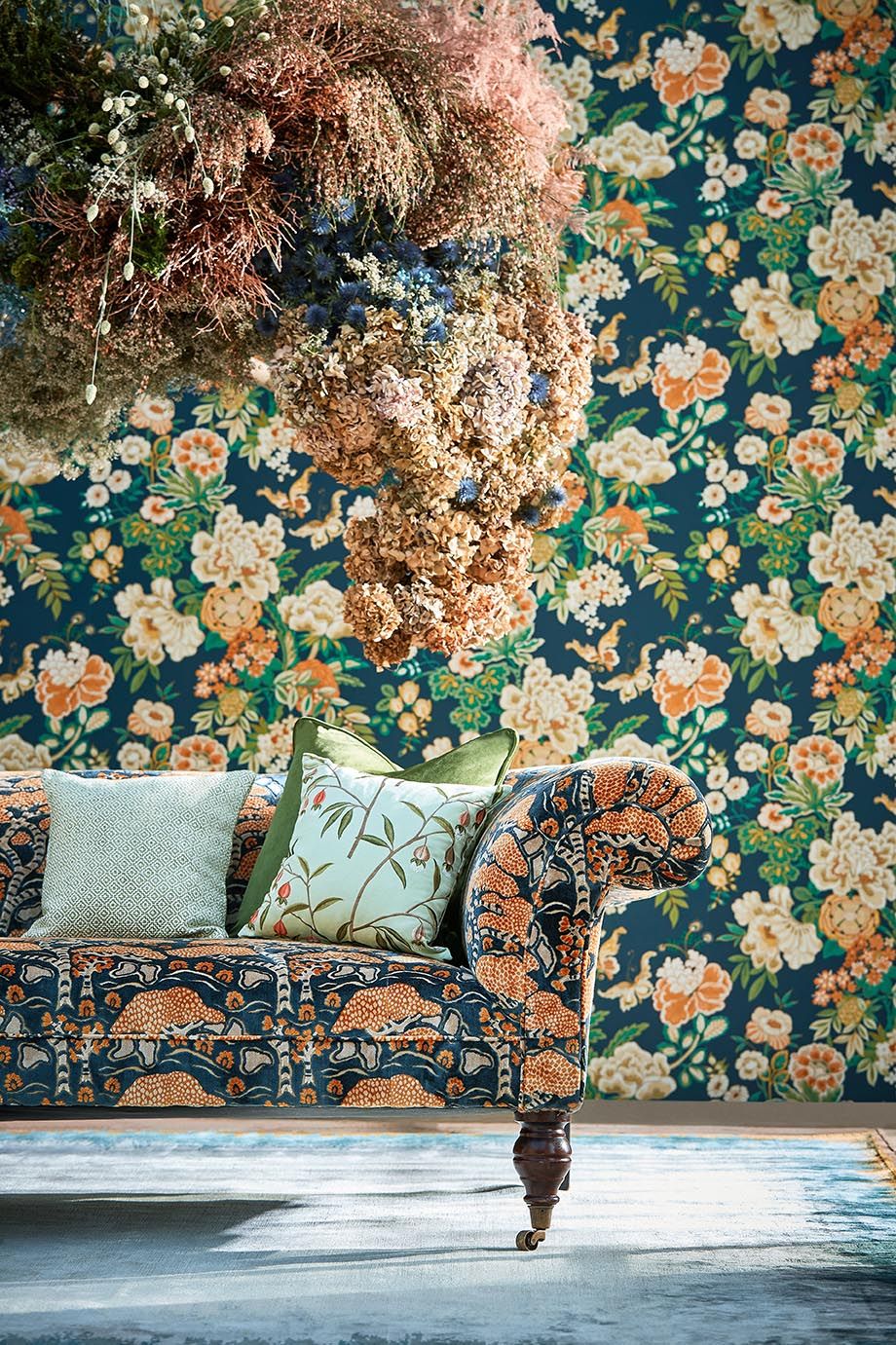 A sofa upholstered in ‘Bonsai amp Gingko cotton velvet in midnightorange is set off by a background of ‘Emperor Peony...