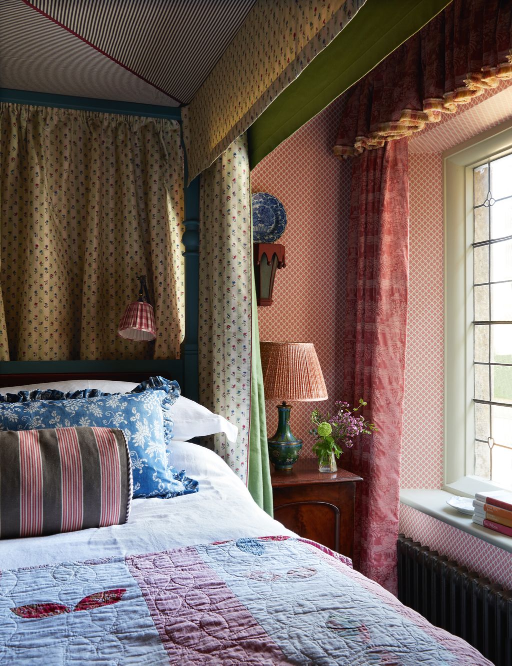 In this bedroom bed curtains in a striped floral from Bennison Fabrics a bolster in Nicole Fabre Designs ‘Lavandou Tabac...