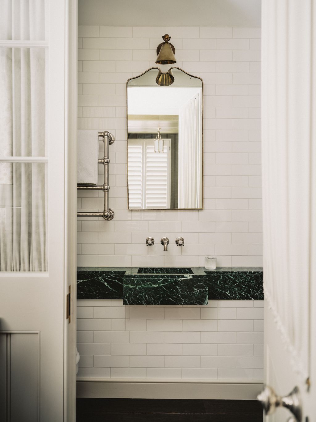 In the guest bathroom an antique brass clipper task wall light by Collier Webb is fixed above a 1970s Italian brass...