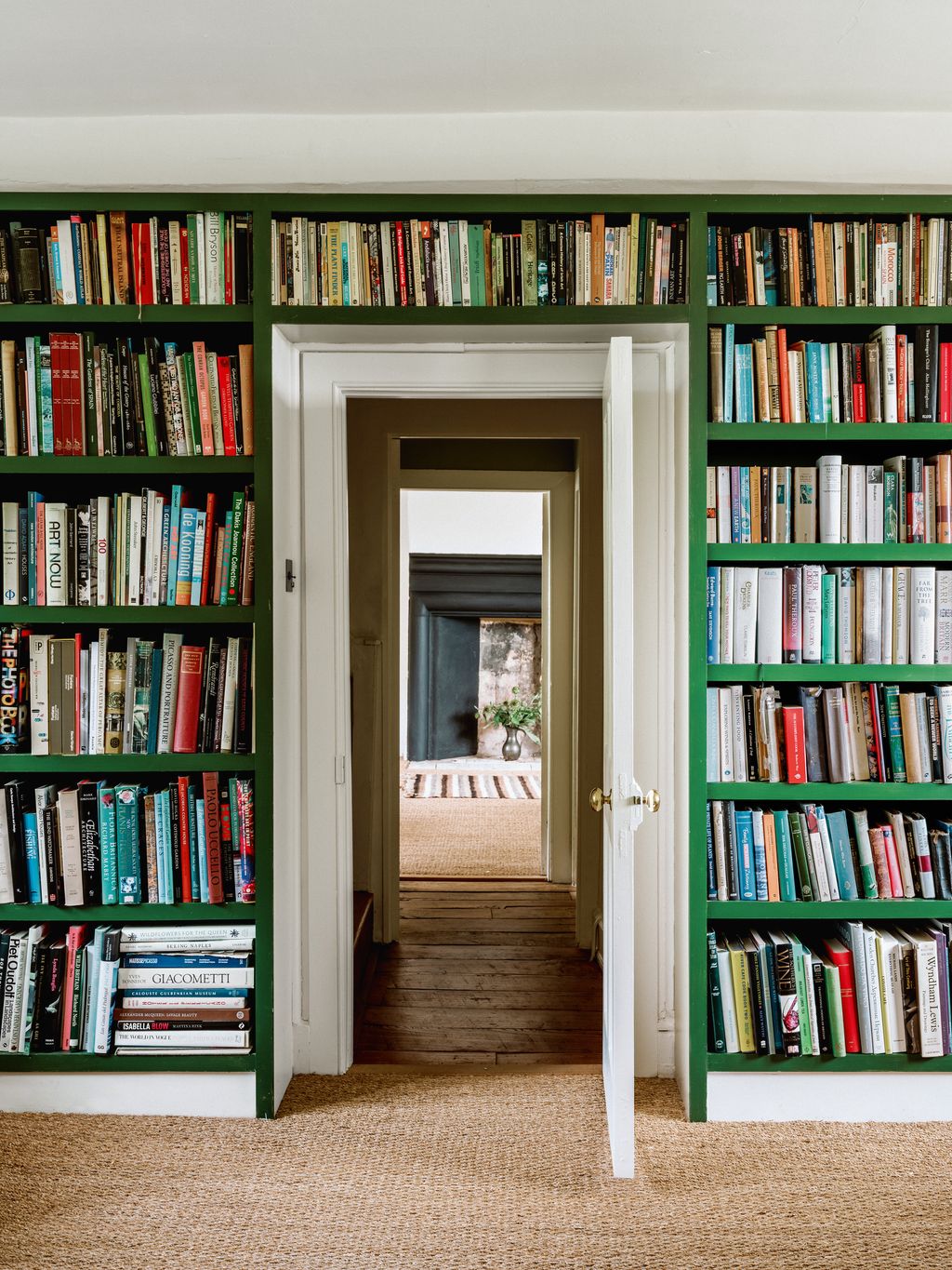Floortoceiling bookshelves in a bespoke green frame the doorway with a view across the hall to a bedroom beyond in...