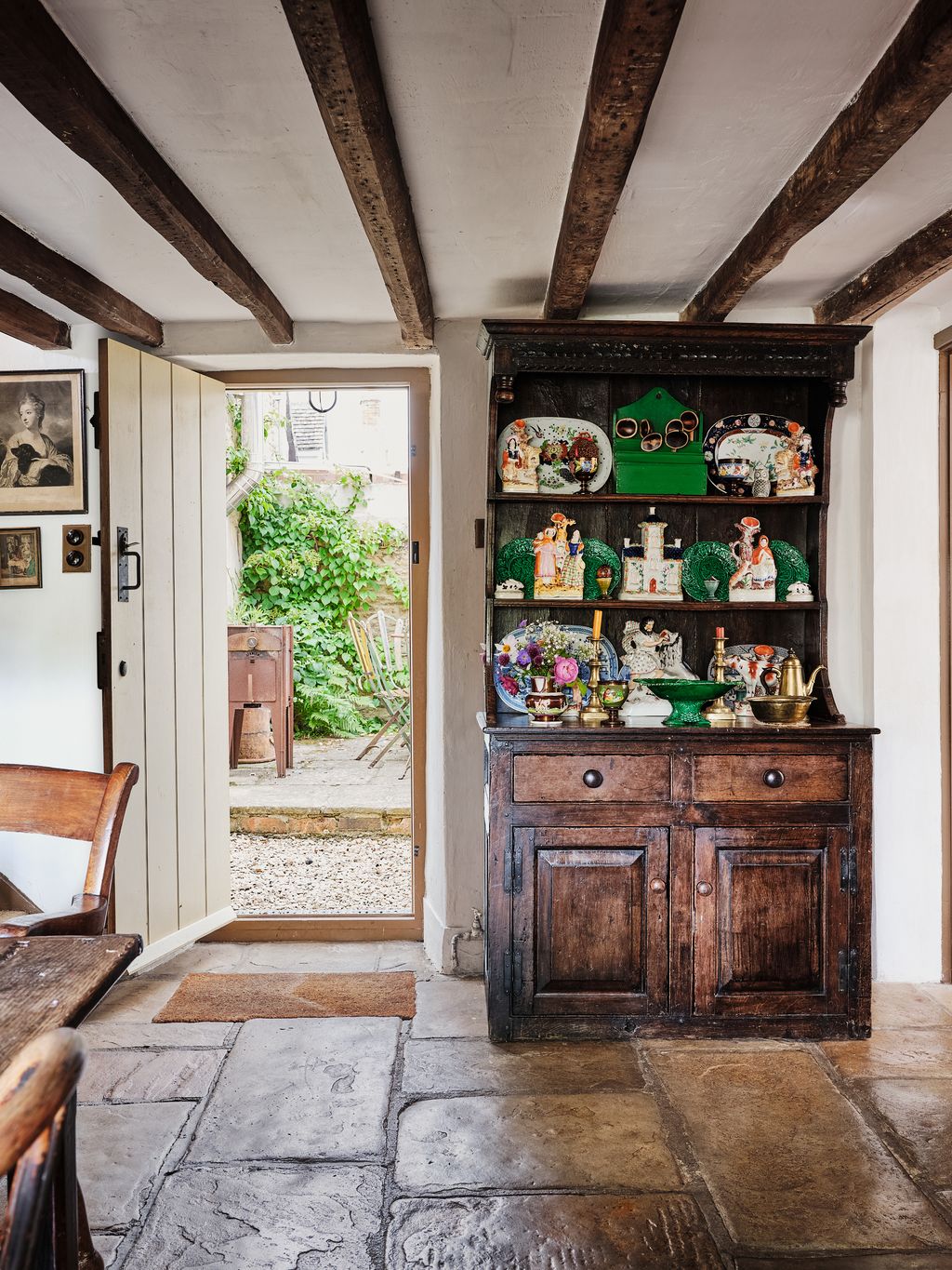A dresser filled with Staffordshire pottery looks out onto the side of the garden where there is a small outdoor dining...