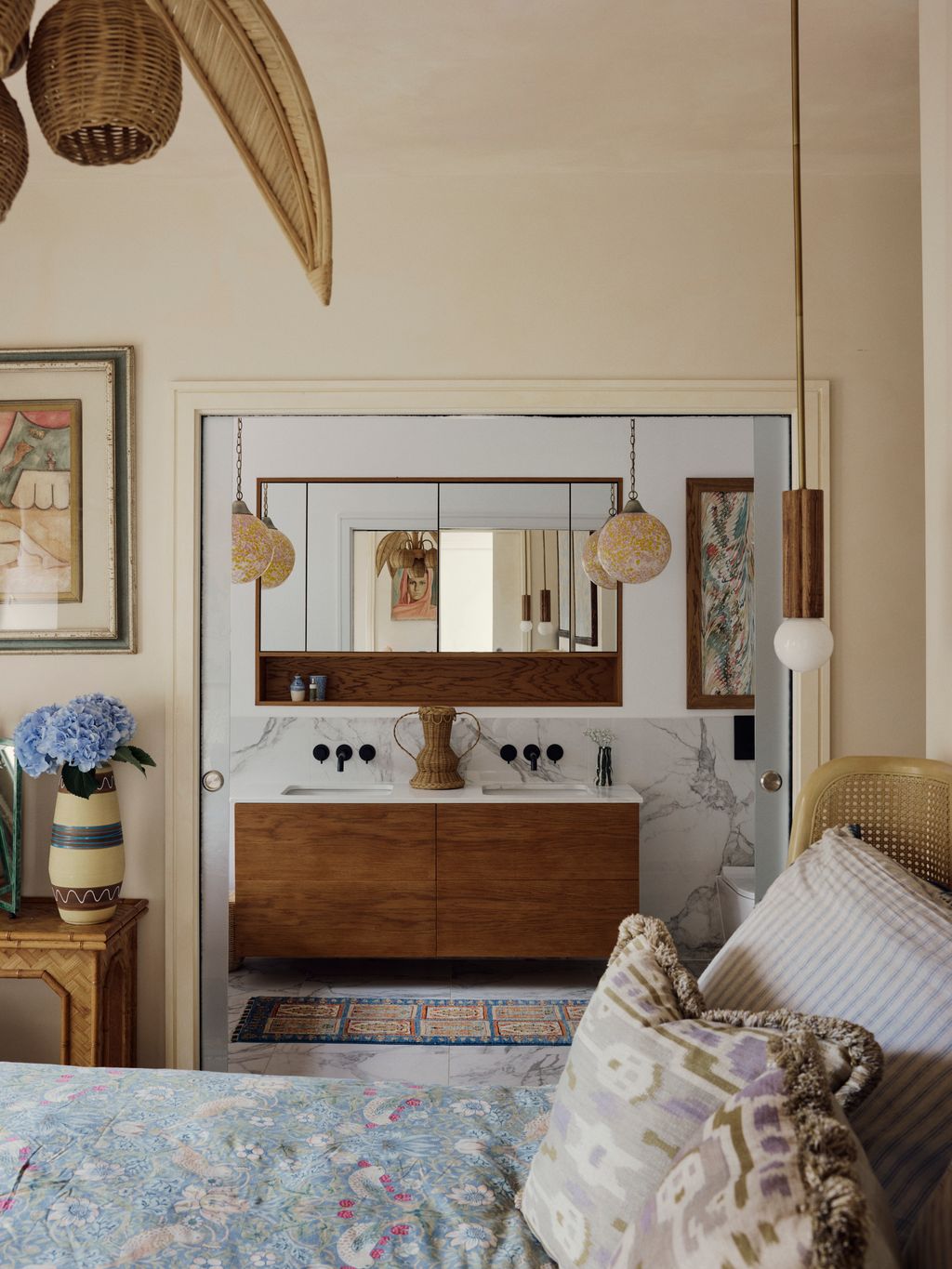 The en suite bathroom is rendered in a calm palette. Murano glass globe lights by Cupla Studio hang above the marble...