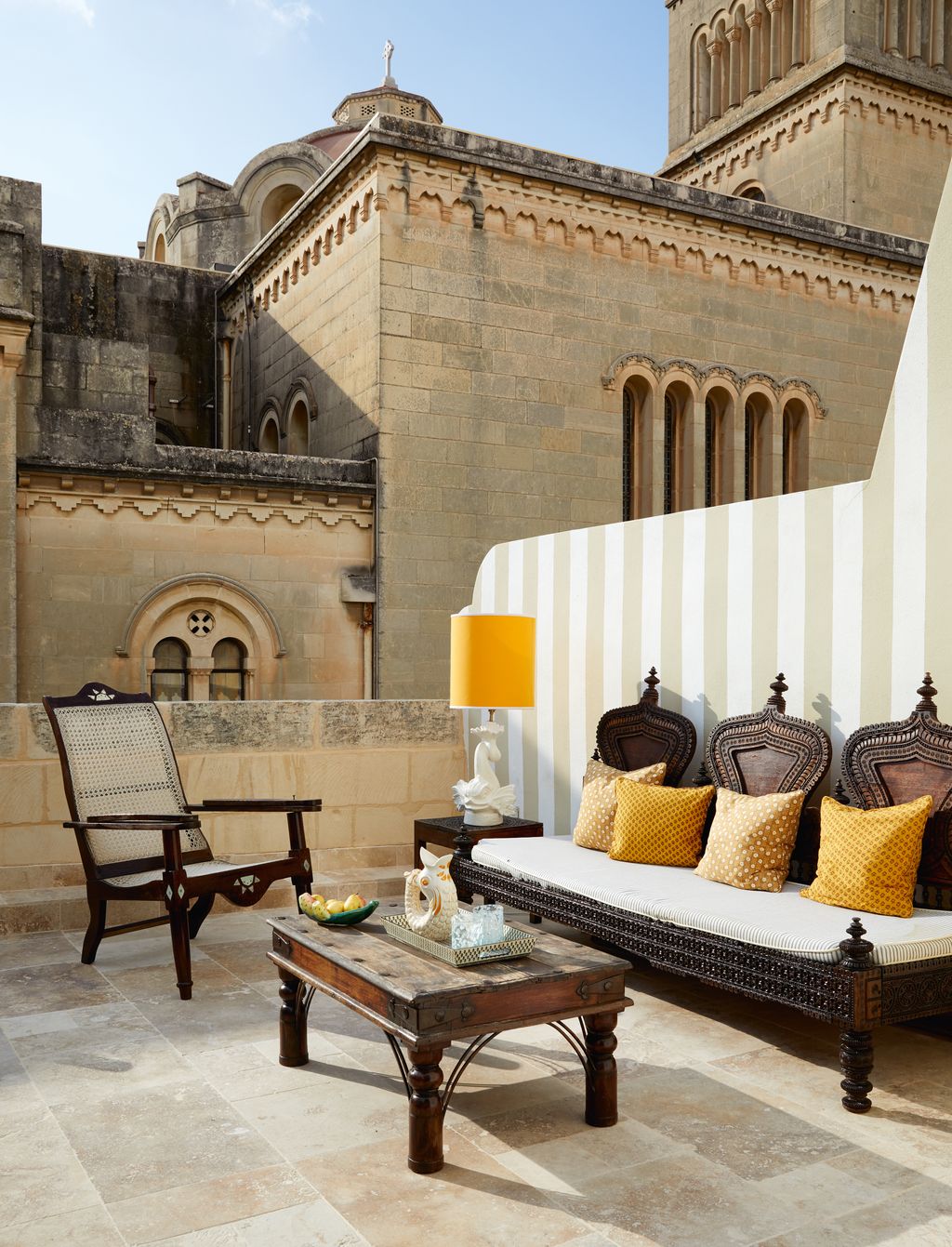 A wall in stripes of white and ‘116 coloured render from Licata showcases an Indian carved bench with cushions in Indian...