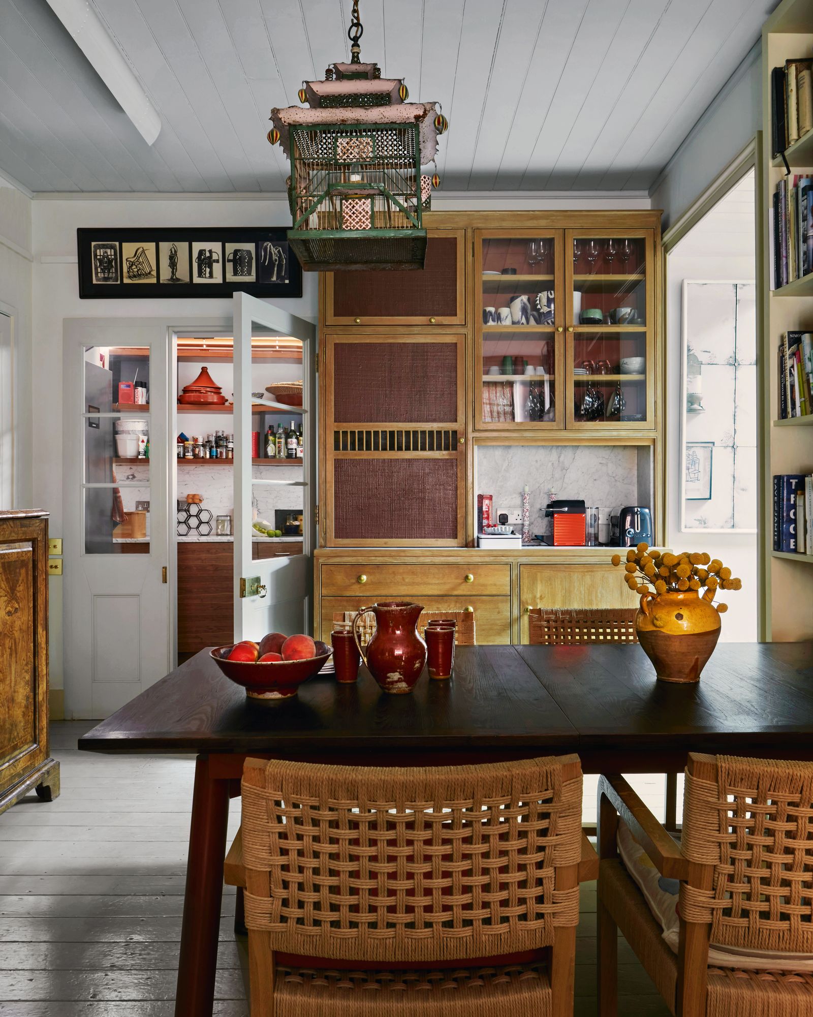 A Victorian tole birdcage converted to a lantern hangs above an extendable table with oak ‘Sled dining chairs by Chester