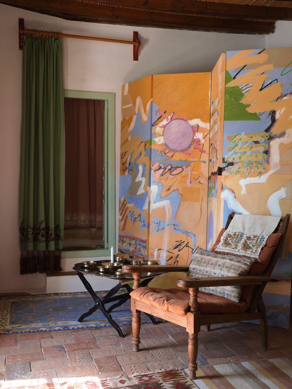 A screen painted by Teddy Millington Drake conceals hanging space. A planters chair is covered in a terracotta cotton.