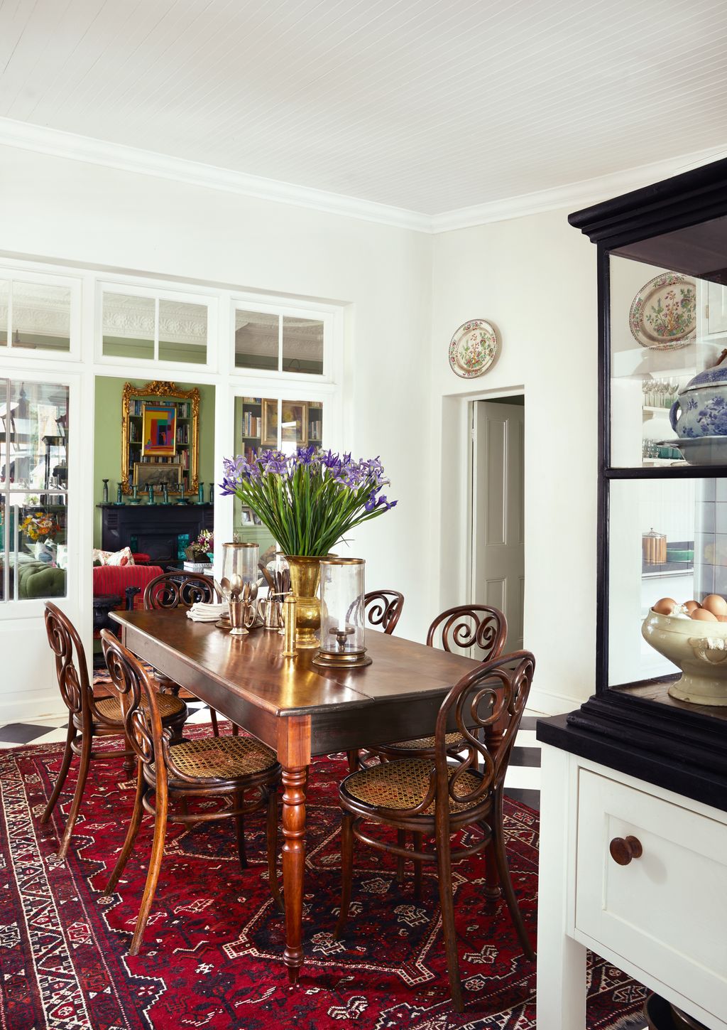 In the kitchen a Persian rug demarcates the dining area where Thonet bentwood chairs surround a teak table. Between a...
