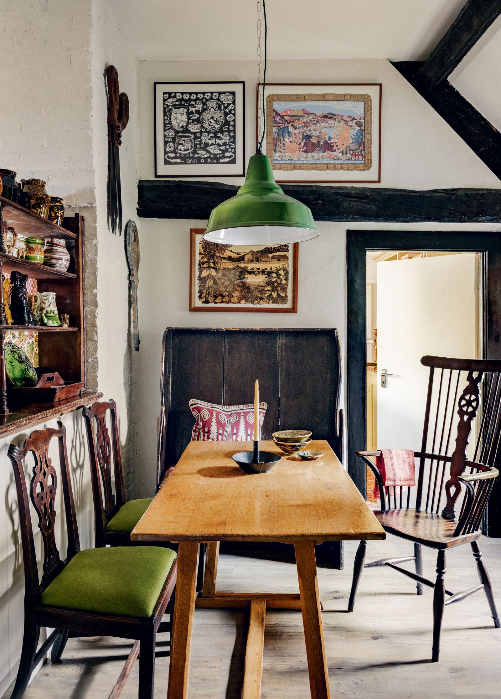 On the wall behind an oak Arts and Crafts table and antique chairs picked up at auctions locally hangs a mix of artworks...