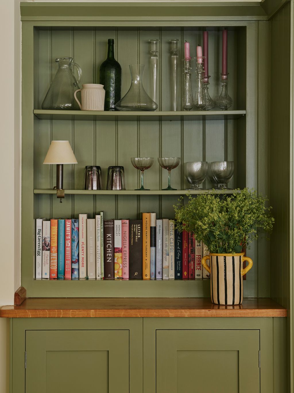 Image may contain Furniture Bookcase Cup Candle Lamp Plant Person and Shelf