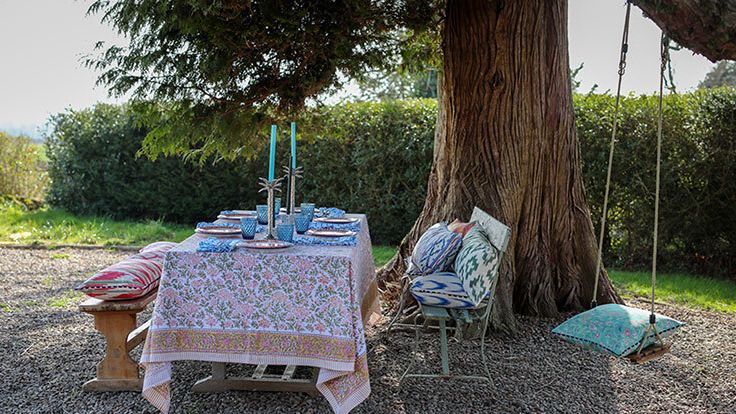 Image may contain: Chair, Furniture, Cup, Grass, Plant, Tree, Home Decor, Desk, Table, Tablecloth, and Bench