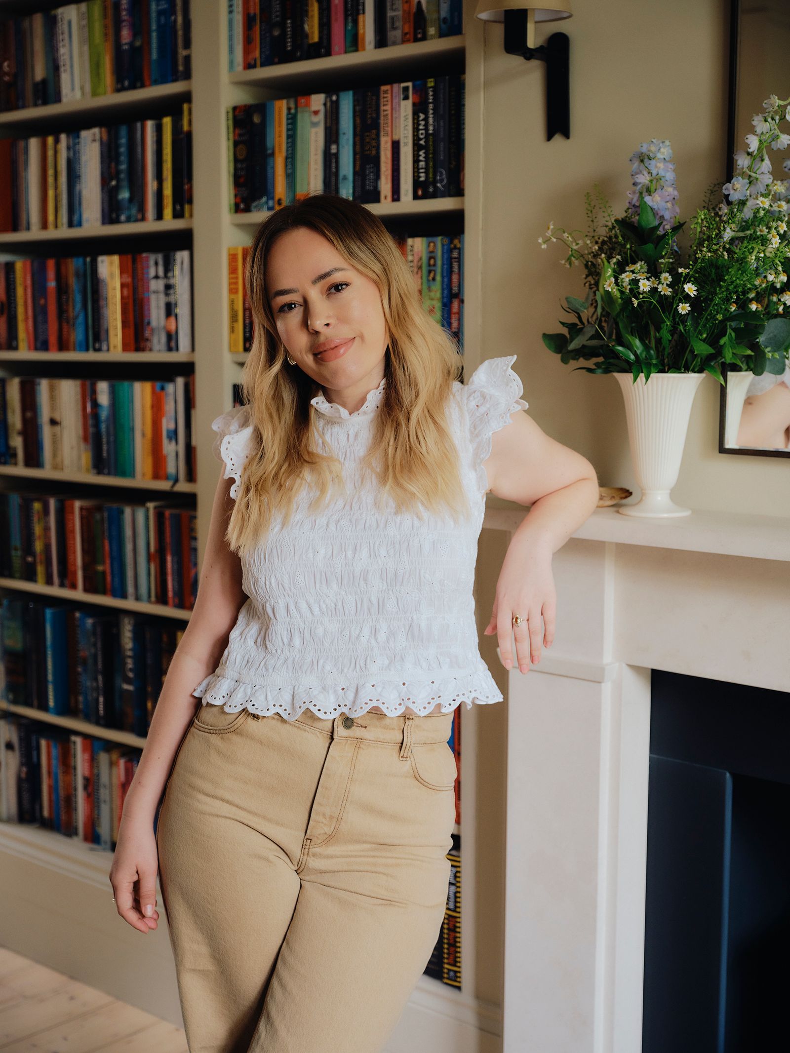 Image may contain Tanya Burr Clothing Sleeve Adult Person Furniture Blouse Bookcase Lamp and Pants