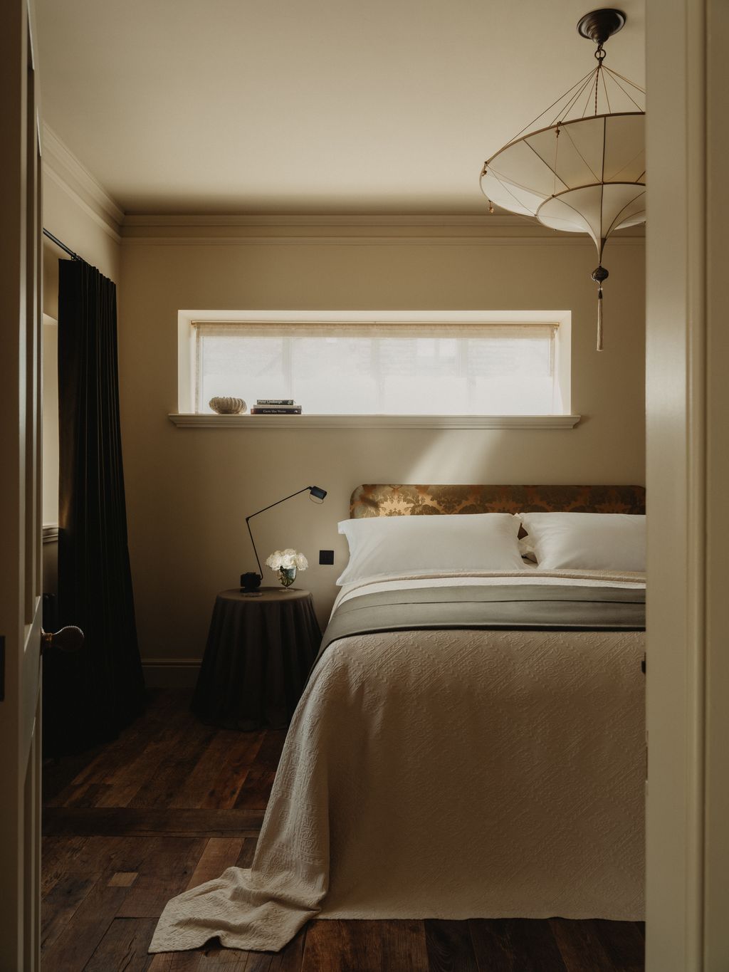 The downstairs bedroom is painted in ‘Canvas IV from Paint  Paper Library. A Fortuny ‘Scheherazade silk lamp hangs...