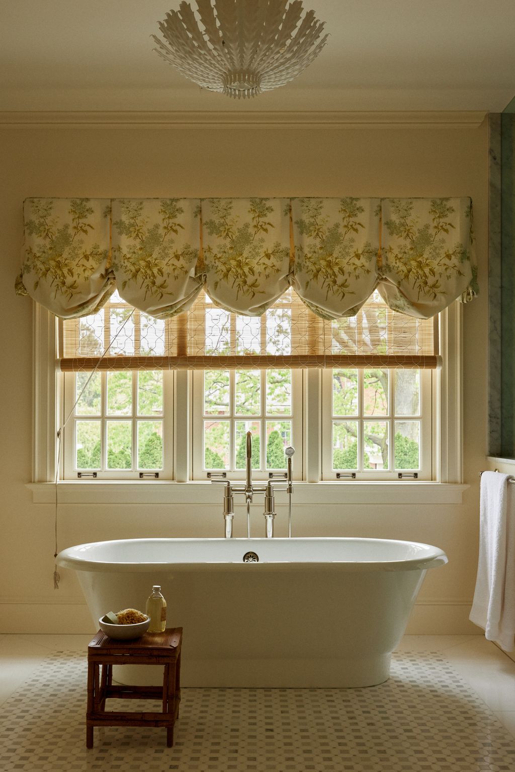 Light pours into this primary bathroom through a trio of sash windows dressed in a curtain by Jasper Fabrics. The deep...
