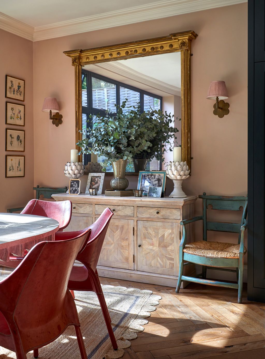 At one end of the kitchen is a dining table surrounded by red chairs from William Yeoward. The mirror above the...
