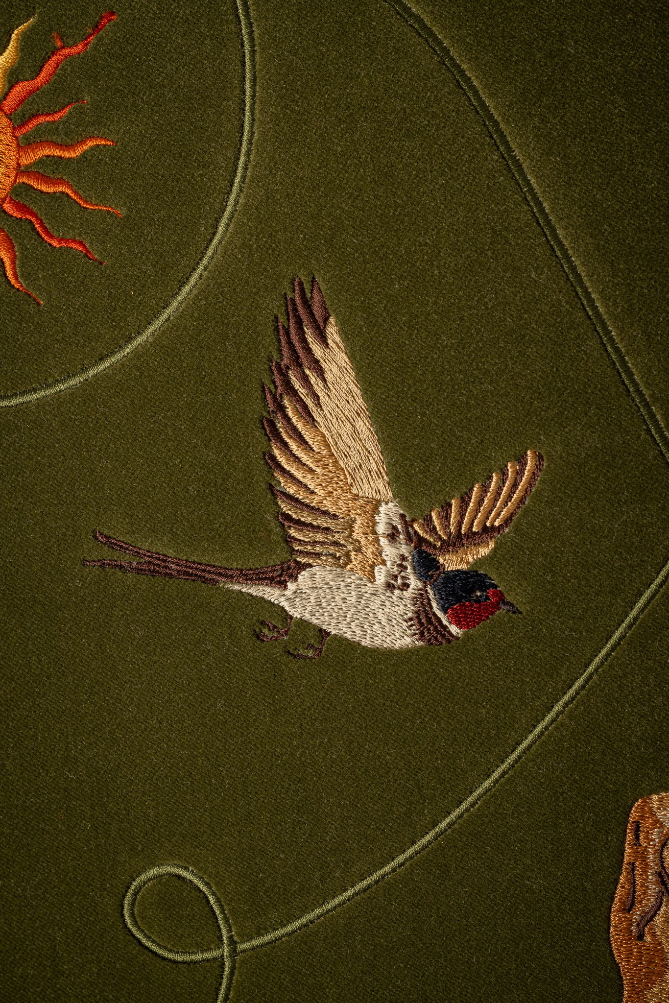 A close up of a motif on ‘Free Me on a walnut footstool covered in juniper coloured velvet fabric