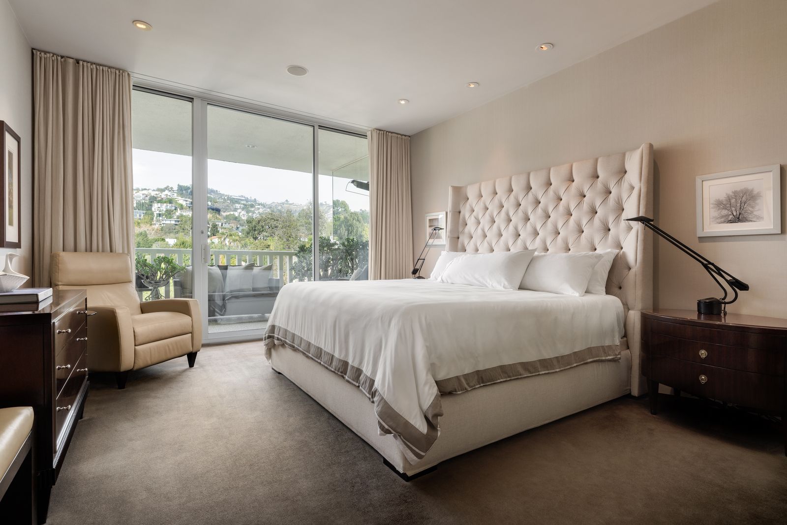 bedroom with beige walls white ceilings beige carpet tall cream tufted headboard white bedding balcony outside glass...