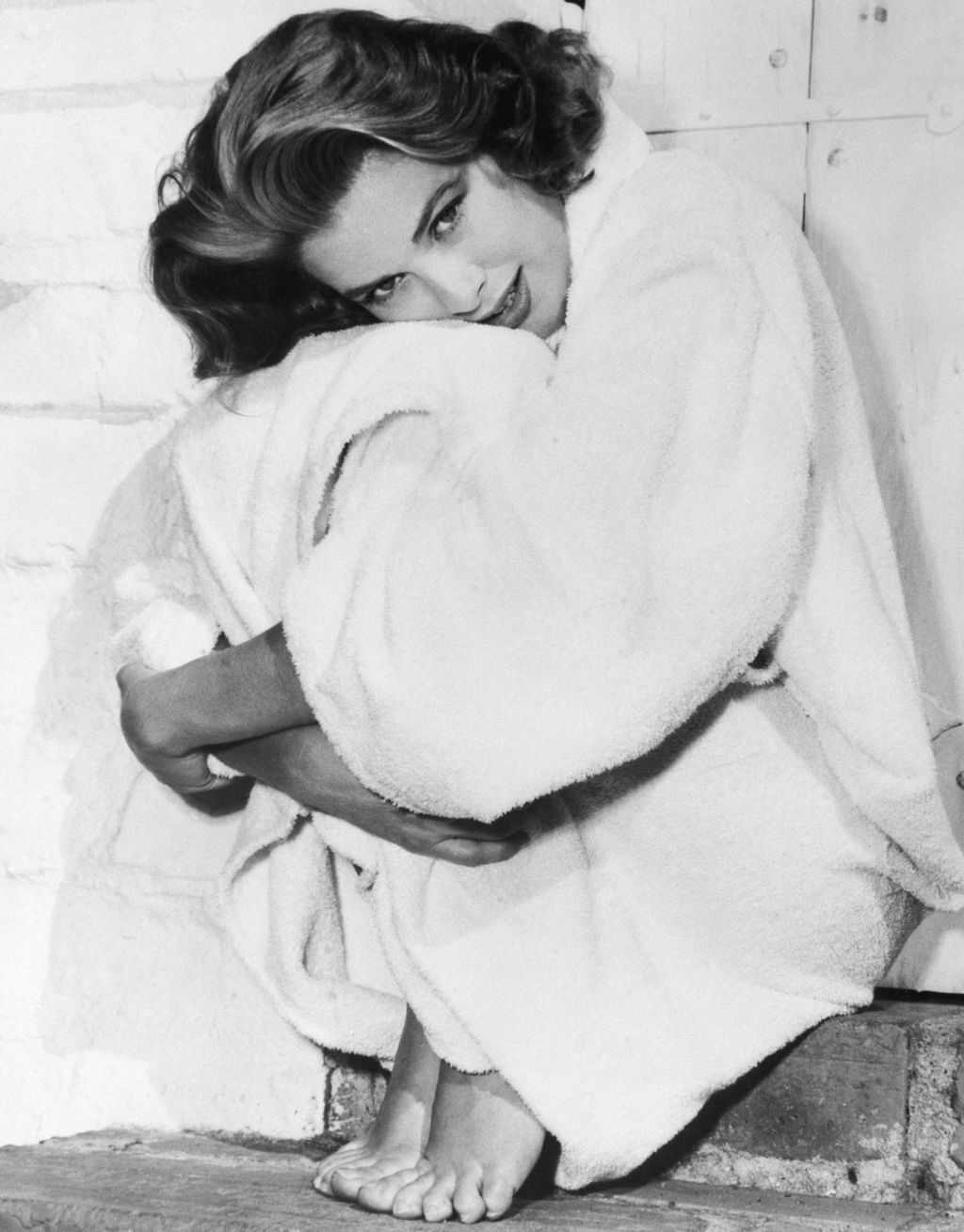 blackandwhite photo of Grace Kelly sat on a stair on tiptoe wearing a robe with her arms wrapped around her legs head...