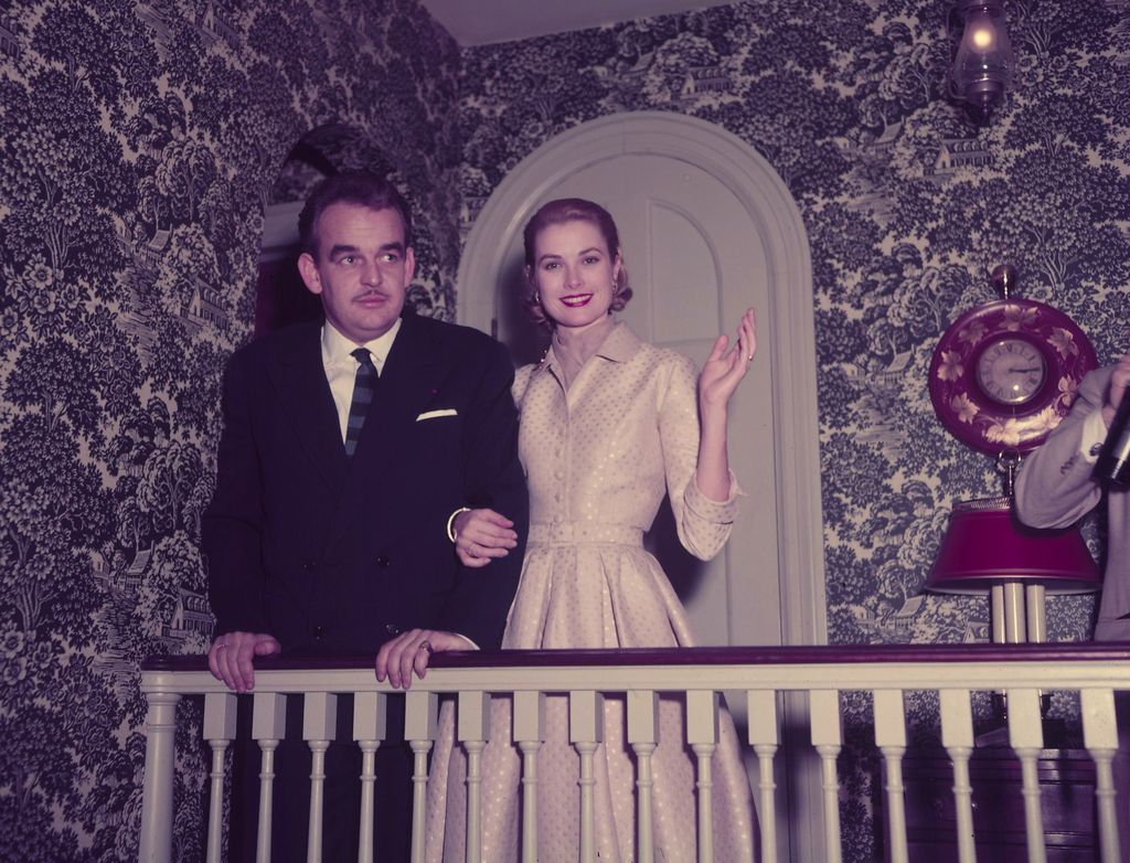 standing along stairway bannister Prince Rainier left and Grace Kelly right smiling and waving with hand in arm of Prince