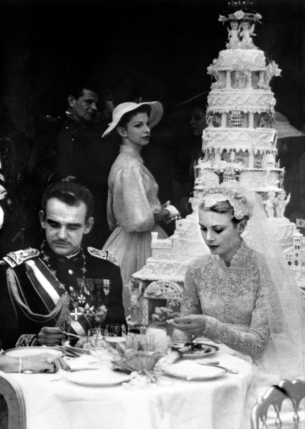 blackandwhite photo of Prince Rainier left seated besides Princess Grace Kelly at their wedding multitiered wedding cake...