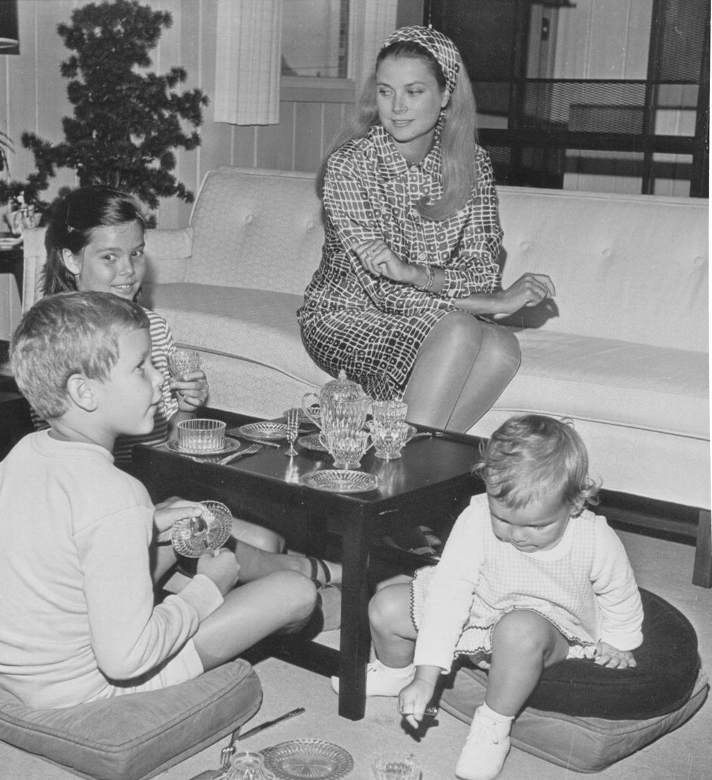 blackandwhite photo of Grace Kelly at home seated on sofa looking down at children seated on floor cushions around the...