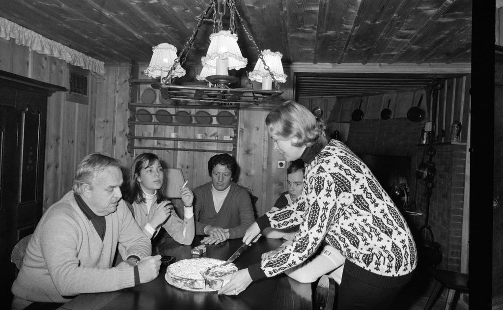 blackandwhite photo of Grace Kelly cutting a dessert for four people sitting around a table in a dining room with low...