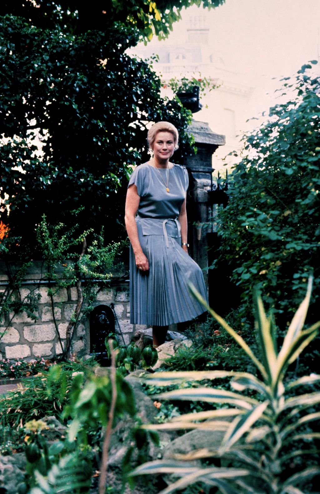 Grace Kelly in blue outfit standing posed in garden