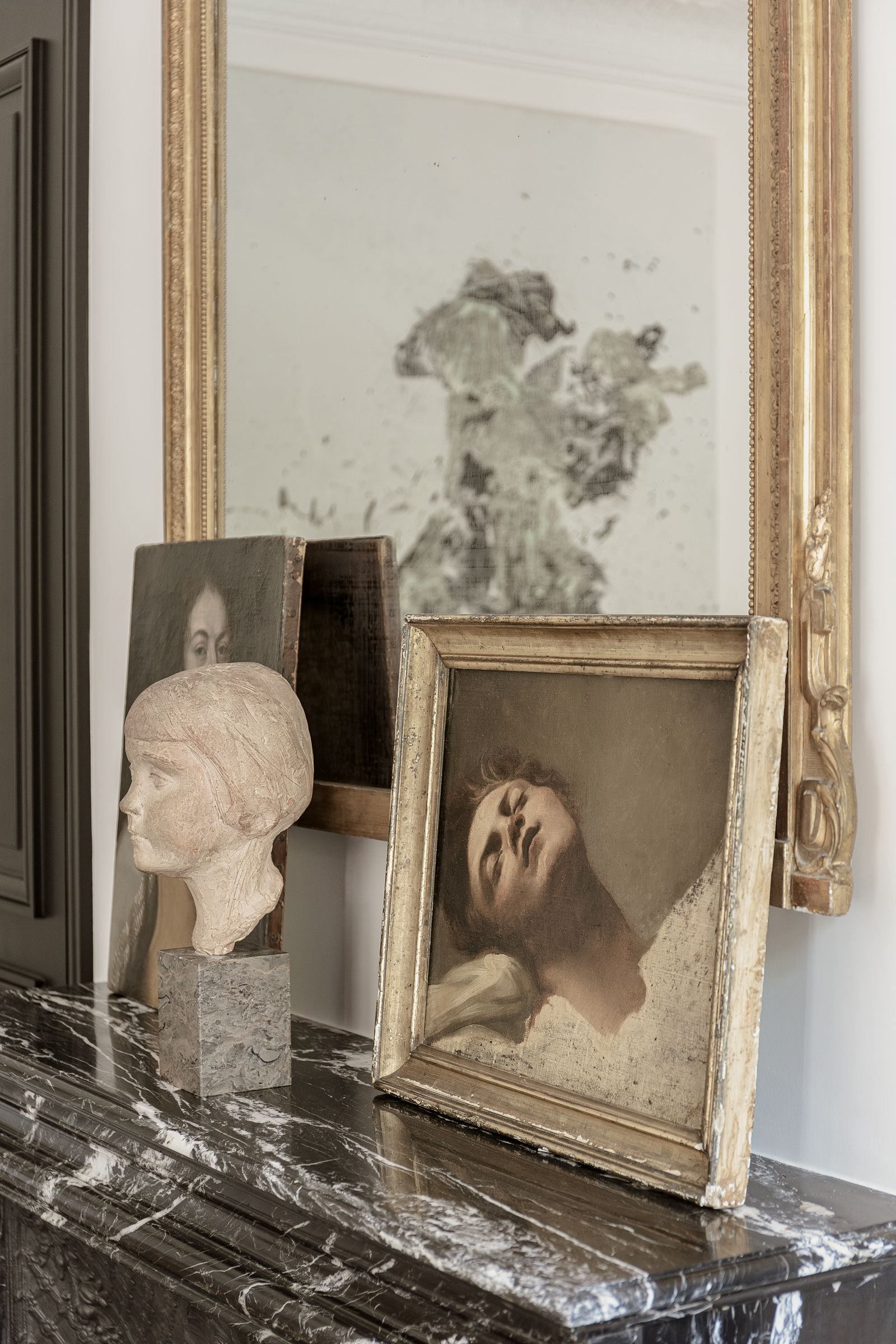 On the mantelpiece in the dining room in front of an antique mirror  are two portraits and a cast bust.