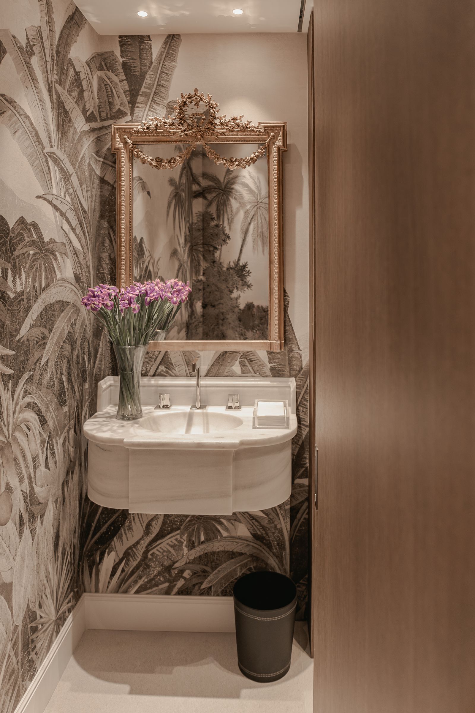 bathroom features a wallpaper in beige and gold tones and a gold framed antique mirror