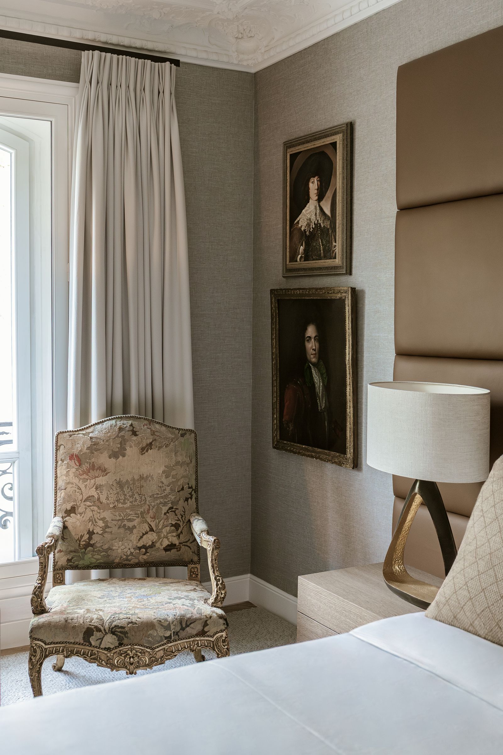 bedroom with light gray walls and bed with leather upholstered headboard and Louis XV armchair